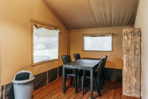 Interno di una tenda safari con tavolo da pranzo, sedie di plastica e pavimento in legno al Familiepark de Vechtvallei, Paesi Bassi.