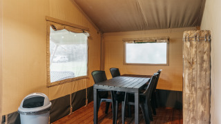 Intérieur d'une tente safari avec table à manger, chaises en plastique et sol en bois à Familiepark de Vechtvallei, Pays-Bas.