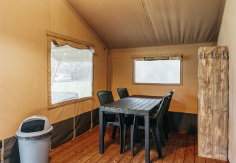 Intérieur d'une tente safari avec table à manger, chaises en plastique et sol en bois à Familiepark de Vechtvallei, Pays-Bas.