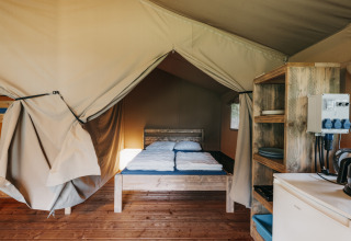 Vista interna di una tenda safari con mobili in legno, letto matrimoniale e cucina nei Paesi Bassi.