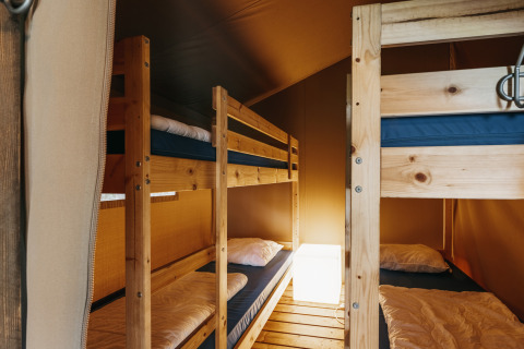 Interno di una tenda safari con letti a castello in legno, biancheria accogliente e luce calda soffusa.