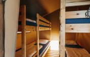 Interior de tienda safari con literas de madera, ropa de cama acogedora y luz cálida ambiente.