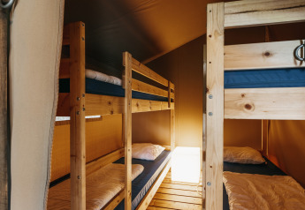 Interior de tienda safari con literas de madera, ropa de cama acogedora y luz cálida ambiente.