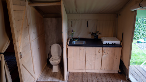 Interior de tienda safari con baño en Camping Emmen, Países Bajos, mostrando cocina y aseo.
