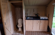 Interior de tienda safari con baño en Camping Emmen, Países Bajos, mostrando cocina y aseo.