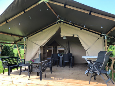 Tenda safari con veranda in legno coperta, mobili da esterno e vista su un ambiente verde.