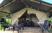 Safari tent with a covered wooden deck, outdoor furniture, and views of lush green surroundings.