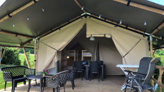 Tenda safari con veranda in legno coperta, mobili da esterno e vista su un ambiente verde.