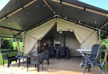Tenda safari con veranda in legno coperta, mobili da esterno e vista su un ambiente verde.