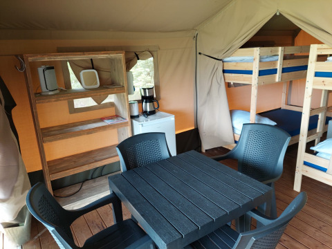 Interior de una tienda safari en Camping Emmen, Países Bajos, con literas, mesa y estanterías de madera.