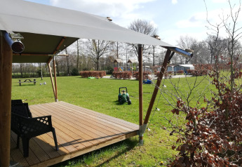 Safari-telt ved Camping Emmen i Holland med overdækket terrasse, græsplæne og legeplads i baggrunden.