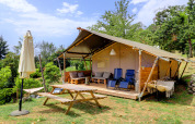 Tienda safari en Camping Pian D'Amora, Italia, con terraza, sillas, mesa de picnic y vegetación alrededor.