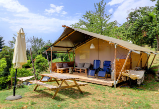 Tienda safari en Camping Pian D'Amora, Italia, con terraza, sillas, mesa de picnic y vegetación alrededor.