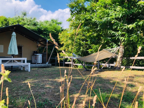 Tienda safari en Camping Pian D'Amora, Italia, con hamaca, árboles y mesa de picnic en un día soleado.