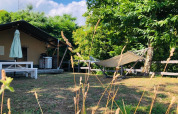 Tienda safari en Camping Pian D'Amora, Italia, con hamaca, árboles y mesa de picnic en un día soleado.