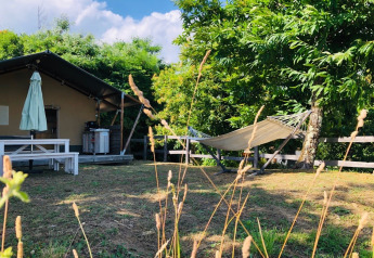 Safari tent at Camping Pian D'Amora, Italy, featuring a hammock, trees, and picnic table on a sunny day.