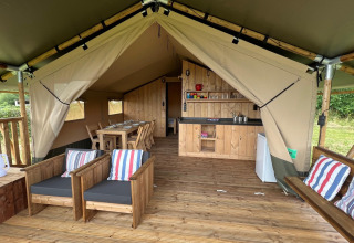 Interior view of a safari tent featuring wooden furniture, dining table, and a small kitchenette area.