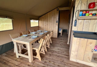 Interior of a safari tent with a wooden dining set, tableware, colorful mugs, and rustic wooden decor.