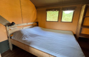 Vista interior de una habitación en una tienda safari con cama doble y ventanas con vistas a la naturaleza.