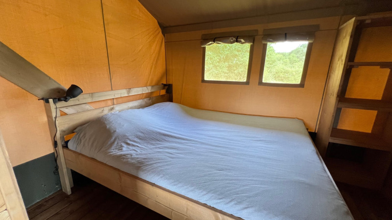 Interno di una camera da letto in tenda safari con letto matrimoniale in legno e finestre sulla natura.