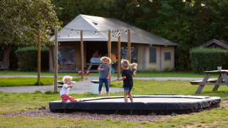 Kinderen spelen op een trampoline voor een safaritent bij FarmCamps Mariekerke vakantiepark in Zeeland.