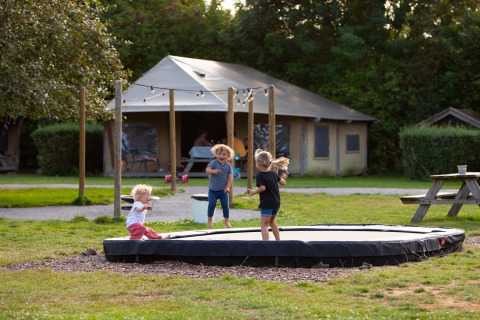 Niños jugando en un trampolín frente a una tienda en FarmCamps Mariekerke, parque de vacaciones en Zeeland.