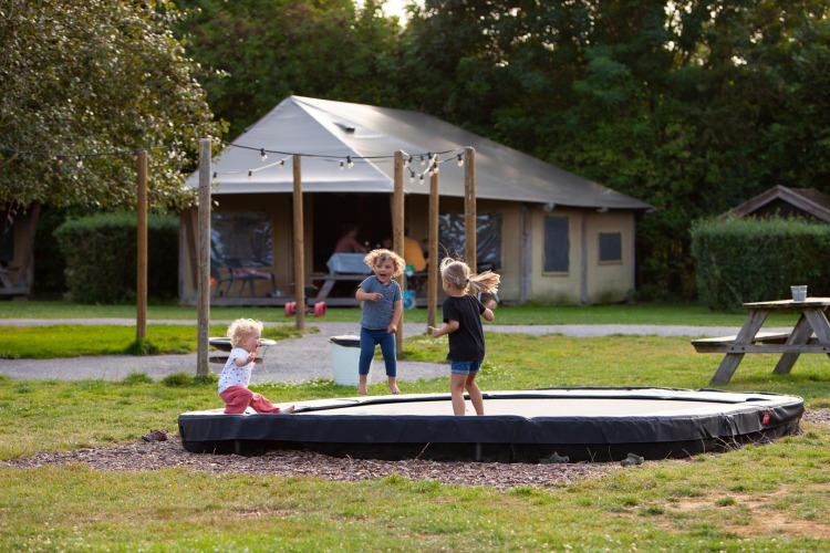Children playing on a trampoline in front of a safari tent at FarmCamps Mariekerke holiday park in Zeeland.