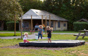 Kinder spielen auf einem Trampolin vor einem Safarizelt im Ferienpark FarmCamps Mariekerke in Zeeland.