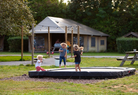 Børn leger på trampolin foran et safaritelt ved FarmCamps Mariekerke feriepark i Zeeland, Nederlandene.