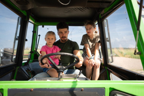 Un hombre con dos niños se sienta dentro de un tractor verde en FarmCamps Mariekerke, un parque vacacional en Zelanda.