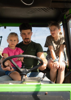 Un hombre con dos niños se sienta dentro de un tractor verde en FarmCamps Mariekerke, un parque vacacional en Zelanda.