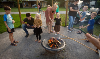 Familias y niños asan malvaviscos sobre una fogata en FarmCamps Mariekerke en Zelanda, Países Bajos.