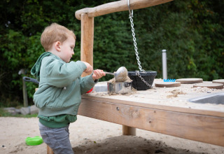 Lille dreng leger med sand og redskaber ved et udendørs legebord på FarmCamps Mariekerke i Zeeland.