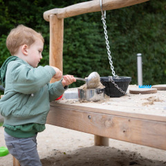 Niño pequeño juega con arena y utensilios en una mesa de juegos al aire libre en FarmCamps Mariekerke, Zeeland.
