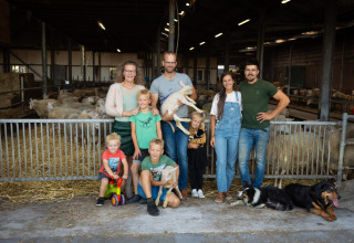 Familie og venner poserer med får, hunde og lam i en lade på FarmCamps Mariekerke i Zeeland, Holland.