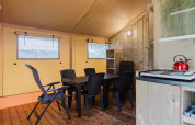 Interieur van een safaritent met eettafel, stoelen en kitchenette bij Familiepark de Vechtvallei.