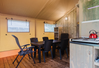 Interior photo of a safari tent with dining table, chairs, and kitchenette at Familiepark de Vechtvallei.