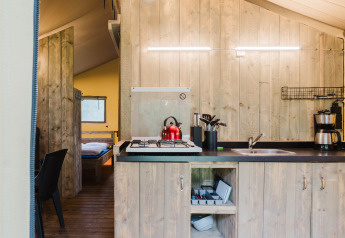 Kitchen in safari tent suite with wooden walls, gas stove, red kettle and coffee maker in Holland.
