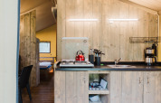Cocina en tienda safari con paredes de madera, estufa de gas, tetera roja y cafetera en Holanda.