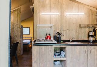 Cucina in tenda safari con pareti in legno, fornello a gas, bollitore rosso e caffettiera in Olanda.