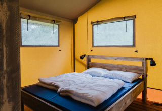 Zona de dormitorio con cama de madera y paredes amarillas en tienda safari en Familiepark de Vechtvallei, Países Bajos.