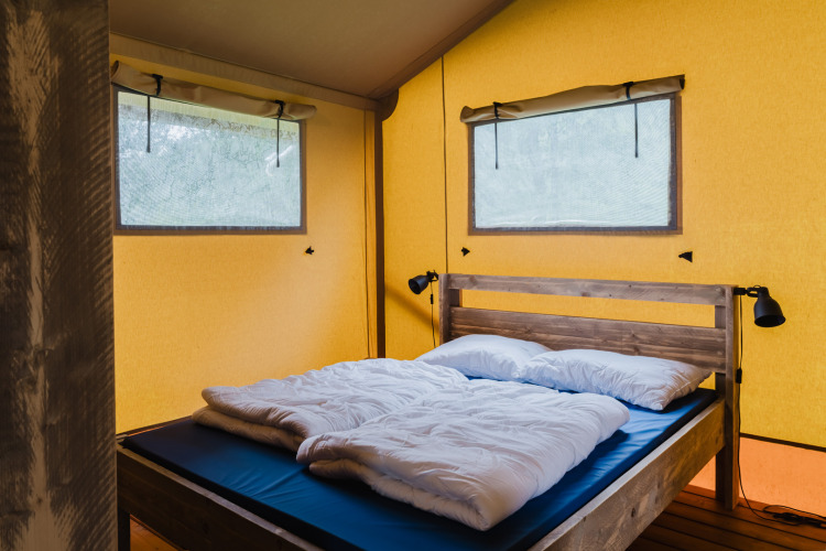 Sleeping area with wood frame bed and yellow walls inside safari tent at Familiepark de Vechtvallei, Netherlands.
