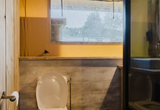 Baño con inodoro, ventana y estilo de madera en una tienda safari en Familiepark de Vechtvallei, Países Bajos.