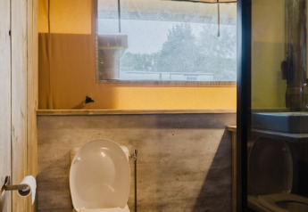 Billede af et badeværelse med toilet, vindue og træbeklædning i en safaritelte ved Familiepark de Vechtvallei.