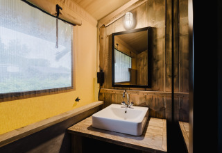 Baño con lavabo, espejo y paredes de madera rústica en tienda safari de Familiepark de Vechtvallei.