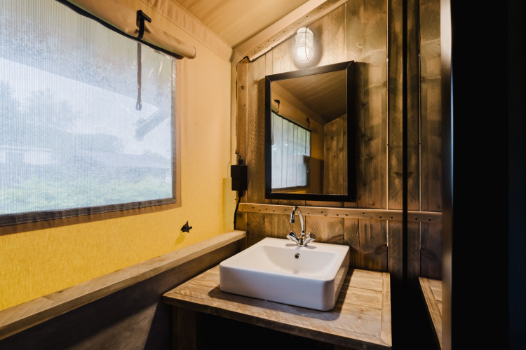 Salle de bain avec lavabo, miroir et murs en bois rustique dans une tente safari à Familiepark de Vechtvallei.