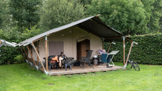Tenda safari con servizi igienici privati, patio esterno, stendino e bicicletta su prato verde.