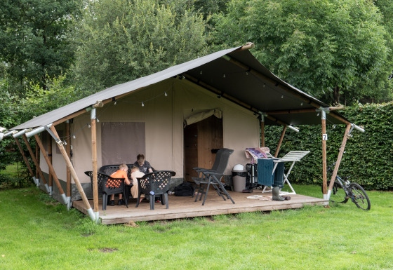 Tenda safari con servizi igienici privati, patio esterno, stendino e bicicletta su prato verde.
