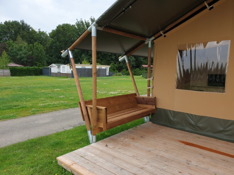 Safari telt med toilet ved Camping Gorishoek i Holland, viser en træveranda og gyngebænk udenfor.