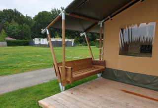 Safari telt med toilet ved Camping Gorishoek i Holland, viser en træveranda og gyngebænk udenfor.